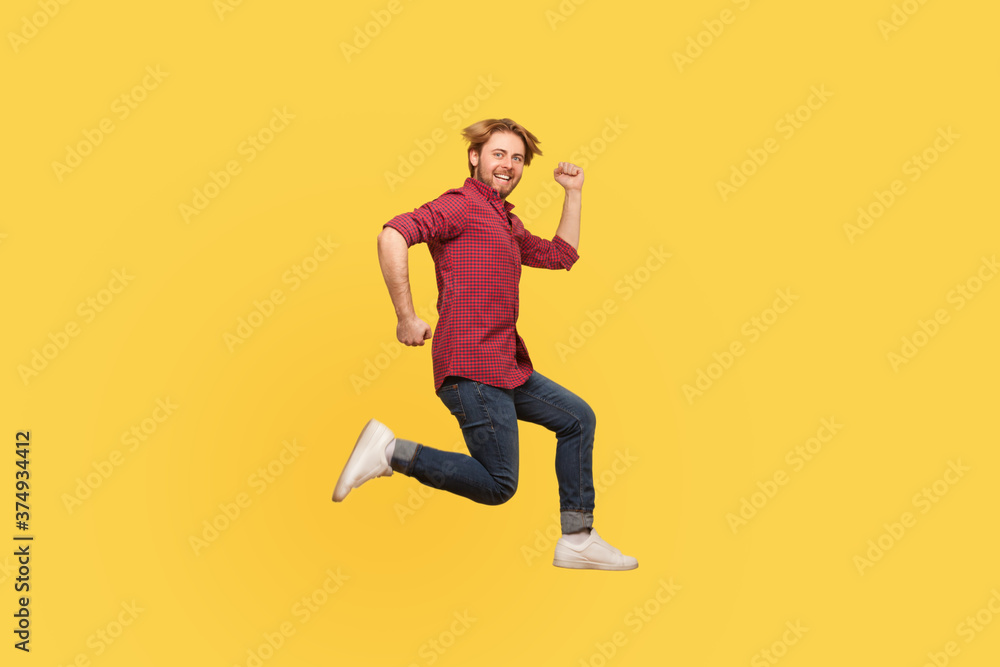 Enthusiastic happy lively guy in casual outfit jumping high trampoline, running fast quickly in air, hurry for sale. Life people energy concept. full length studio shot isolated on yellow background