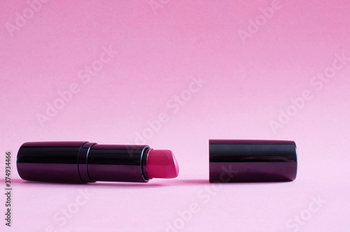 An old used tube of lipstick lies on pink background