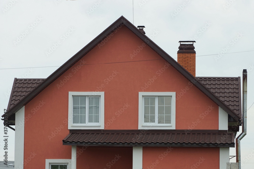 facade of a red private house with white windows under a brown tiled roof against a gray sky facade of a red private house with white windows under a brown tiled roof against a gray sky