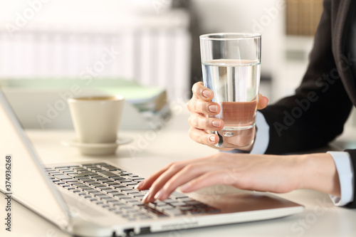 Executive hands holding water glass using laptop at office