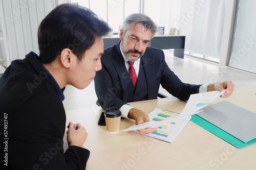 Senior male manager and his Asian colleague meeting and analyzing data and sales record documents of the company in the office Business planning and working lifestyle concept