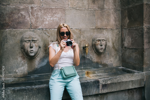 Happy Caucasian female amateur testing retro camera for editing images during solo journey trip, carefree woman tourist in stylish sunglasses checking vintage equipment with photo pictures