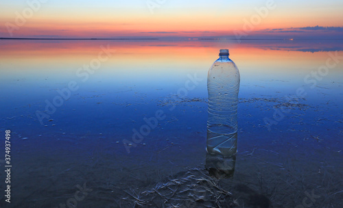 Plastic bottle in water on sunset background