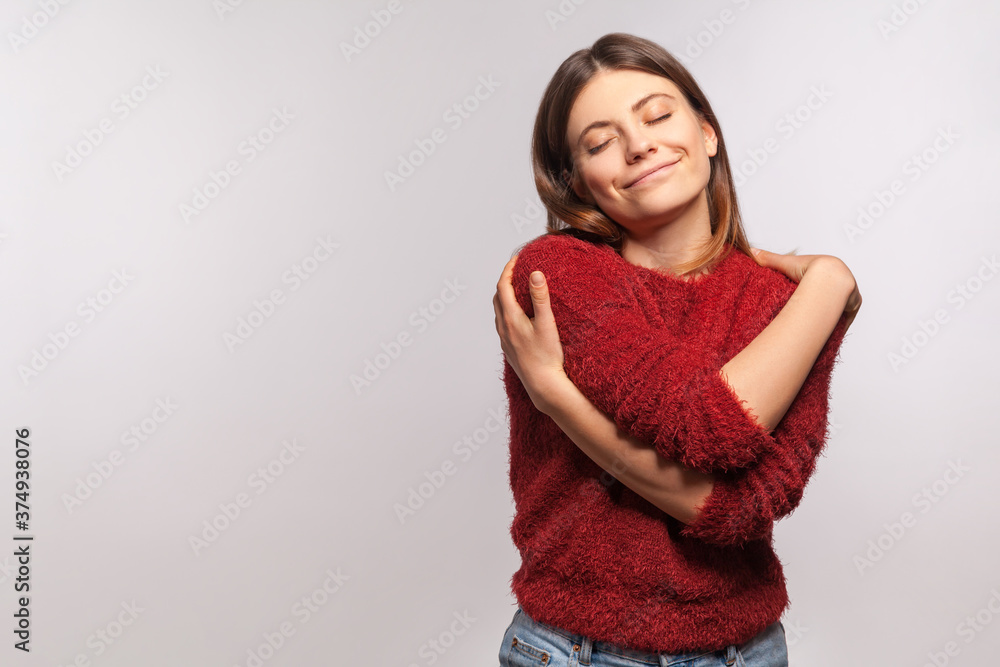 I love myself! Portrait of narcissistic selfish girl in shaggy sweater embracing herself, closed eyes and smiling with pleasure, complacency and egoism concept. studio shot isolated on gray background - obrazy, fototapety, plakaty 