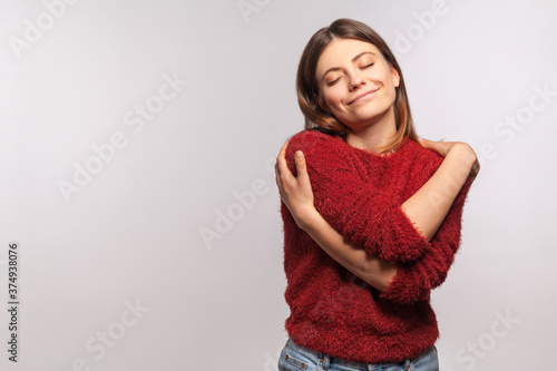 I love myself! Portrait of narcissistic selfish girl in shaggy sweater embracing herself, closed eyes and smiling with pleasure, complacency and egoism concept. studio shot isolated on gray background