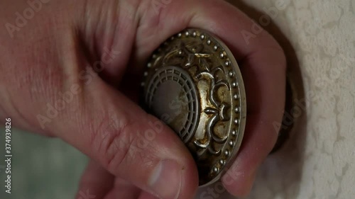 A man's hand touches a round metal doorknob. A man opens a wooden door painted with white paint in the house by a decorative handle. Household items