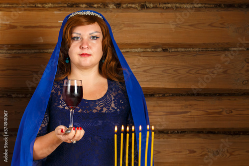 On the eve of Rosh Ashan, a Jewish woman stands next to burning candles with a glass of Kiddush wine in her hand. photo