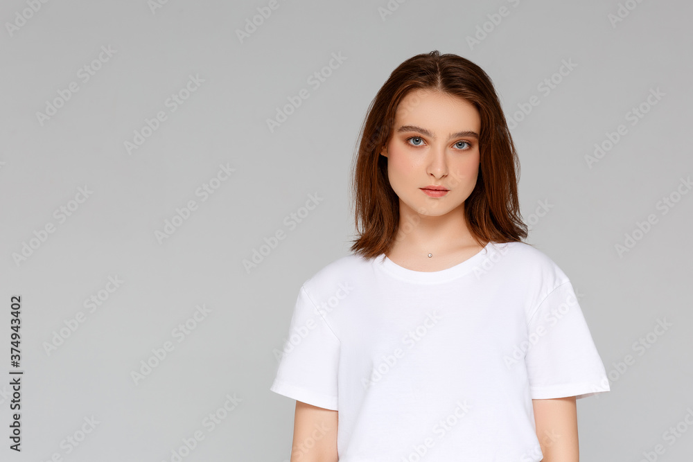 Close up portrait of smiling young woman in white t-shirt looking at camera, isolated on gray background Close up portrait of smiling young woman in white t-shirt looking at camera, isolated on gray background