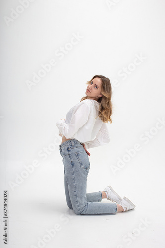 portrait of young caucasian woman with long hair in shirt, jeans, isolated on white studio background. pretty girl posing. attractive female standing on her knees on floor