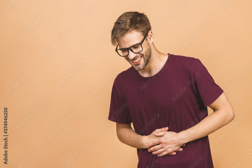 Young man in pain holding his hurting stomach isolated on the beige background. Abdominal pain. Young man in pain holding his hurting stomach isolated on the beige background. Abdominal pain.