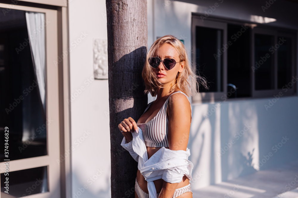 Fototapeta premium Woman in bikini and whire shirt on vacation outside villa hotel, natural sunset light. 