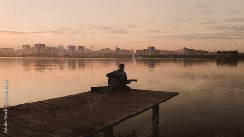 The young man playing guitar beside a lake with sunset