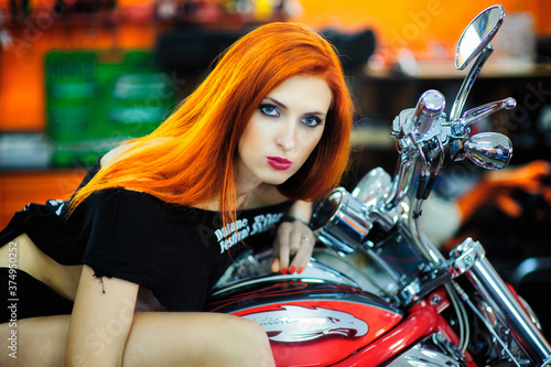 Portrait of charming young woman with red hair near a motorcycle