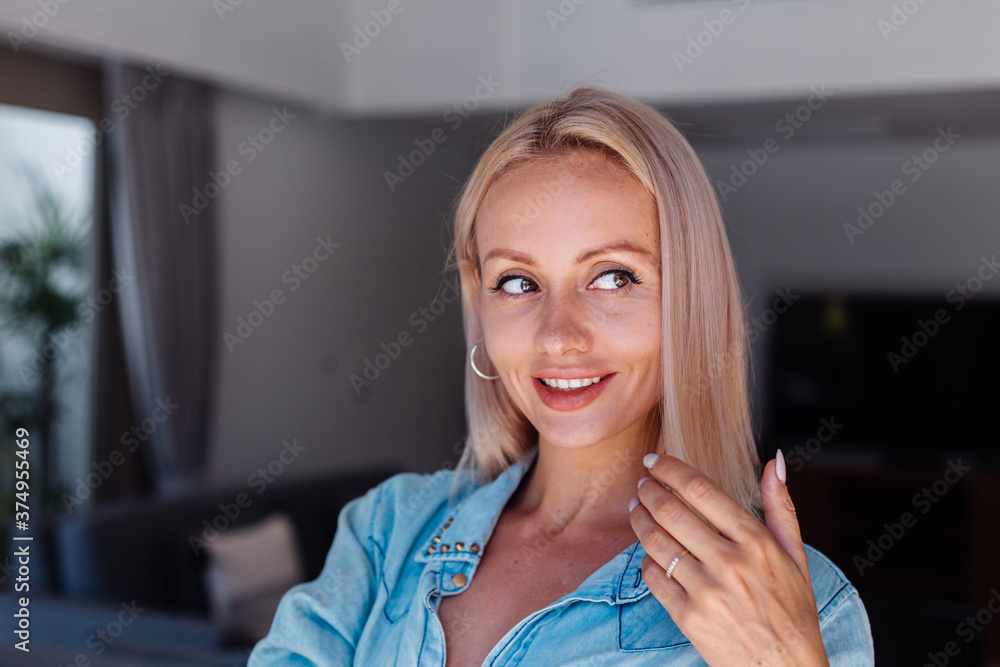 Caucasian pretty blonde short hair woman in denim jacket brushing hair with pink hairbrush in living room Caucasian pretty blonde short hair woman in denim jacket brushing hair with pink hairbrush in living room