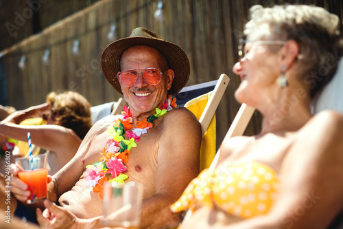 Group of cheerful seniors sitting by swimming pool outdoors in backyard, party concept.