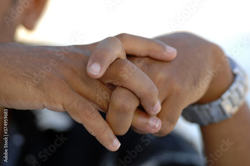 A brown skinned man with crossed fingers. A relaxed hand position. 