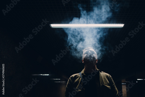 Portrait of young caucasian man smoking e-cigarette in dark with line light