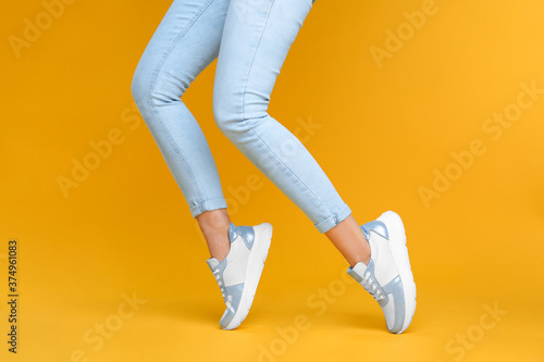 Woman wearing stylish sneakers on yellow background, closeup