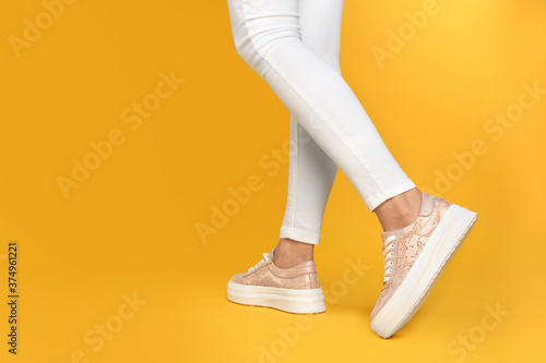 Woman wearing stylish shoes on yellow background, closeup. Space for text