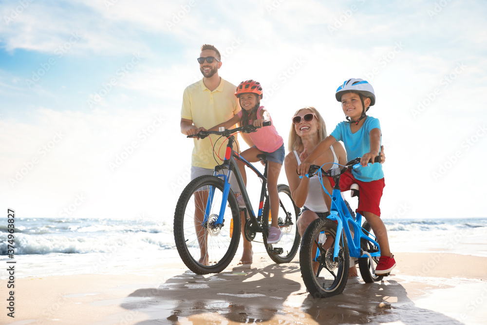 Fototapeta premium Happy parents teaching children to ride bicycles on sandy beach near sea