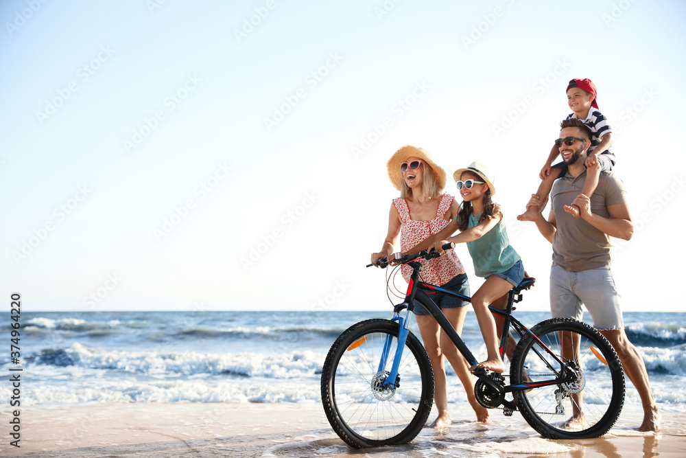 Fototapeta premium Happy family with bicycle on sandy beach near sea