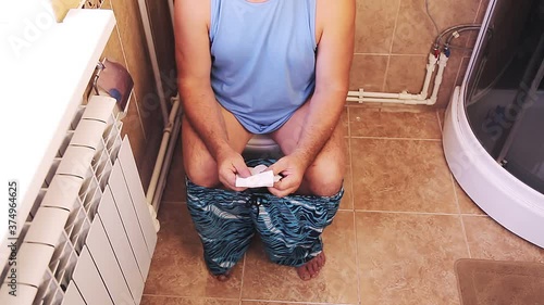 A man in shorts and glasses in the toilet sits on the toilet without a face
