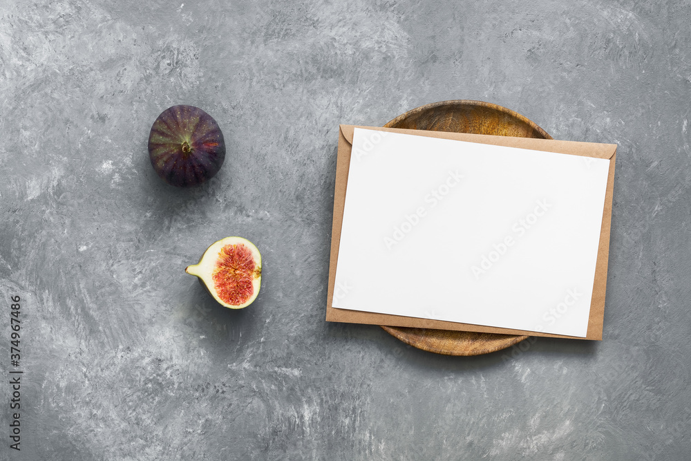 Blank paper card mockup with envelope on wooden plate and fresh figs. Gray concrete background. Company corporate identity template. Modern minimal still life. Top view, flat lay Blank paper card mockup with envelope on wooden plate and fresh figs. Gray concrete background. Company corporate identity template. Modern minimal still life. Top view, flat lay