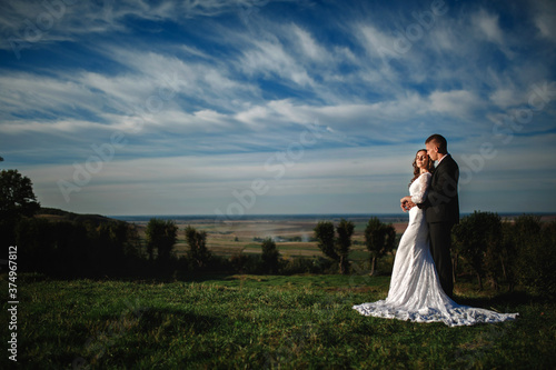 elegant groom hugs a gorgeous brunette bride on a background of nature and blue sky