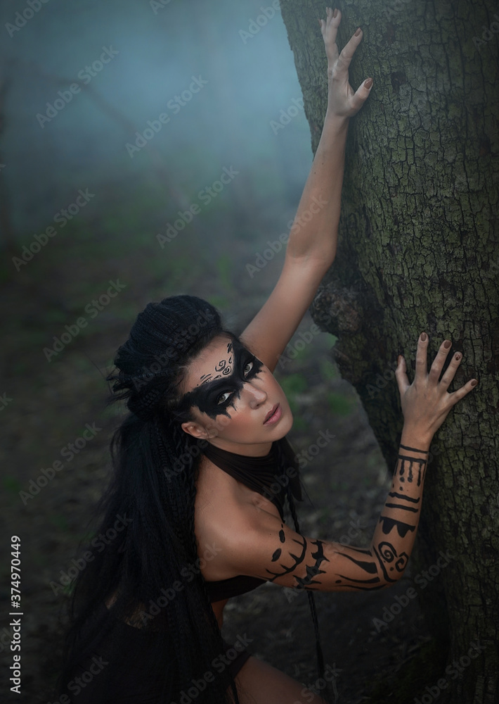 Portret close up of beautiful tribal shaman woman in a foggy forest. Hands of ethnic dancer.Amazon girl near the tree. Soft focus