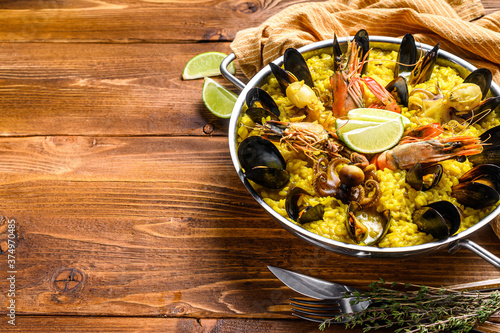 Seafood paella in the fry pan with prawns, shrimps, octopus and mussels. Wooden background. Top view. Copy space