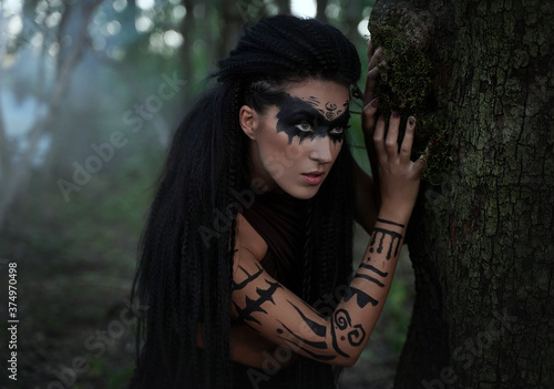 Portret close up of beautiful tribal shaman woman in a foggy forest.Amazon girl near the tree. Soft focus