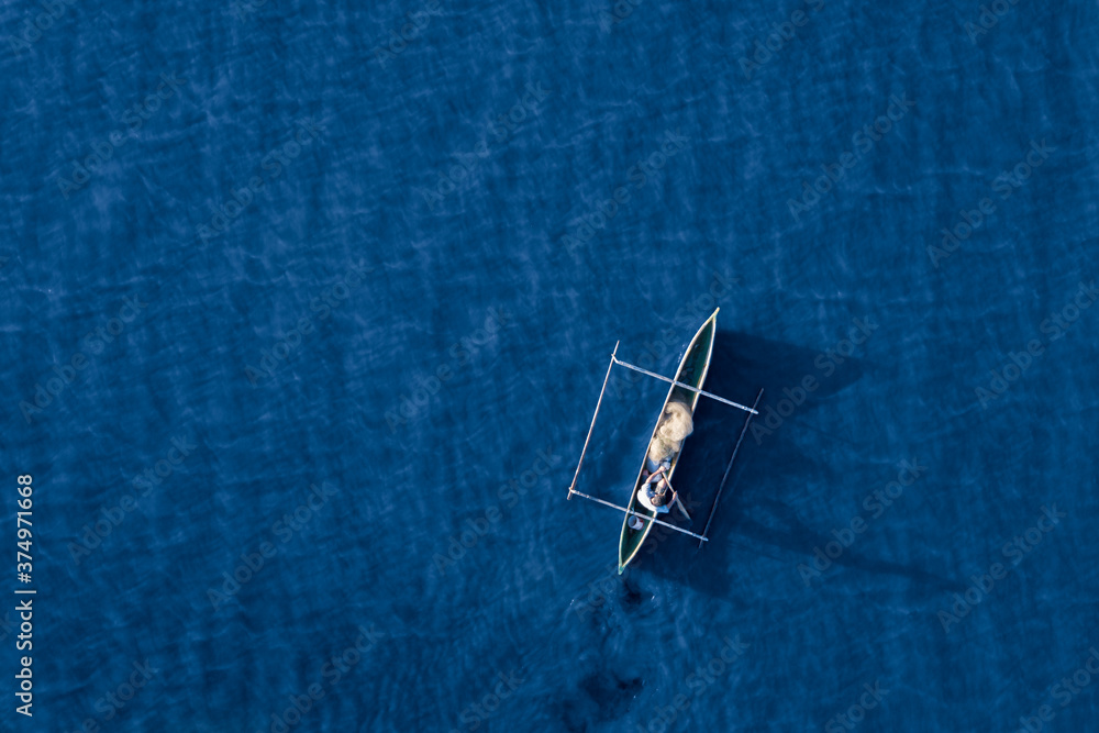 Aerial view of a fisherman and his mirror shadow fishing using a pirogue boat on deep blue ocean waters during sunrise in Dili, Timor-Leste Aerial view of a fisherman and his mirror shadow fishing using a pirogue boat on deep blue ocean waters during sunrise in Dili, Timor-Leste