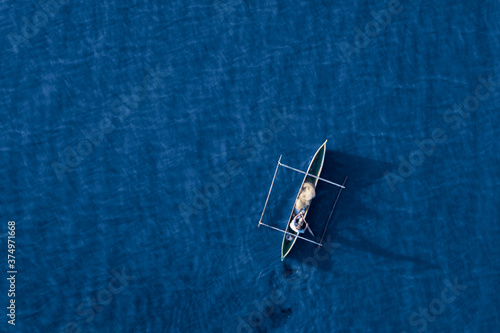 Aerial view of a fisherman and his mirror shadow fishing using a pirogue boat on deep blue ocean waters during sunrise in Dili, Timor-Leste
