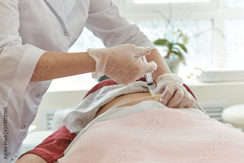 Doctor in white coat and gloves gives an injection into patient stomach.