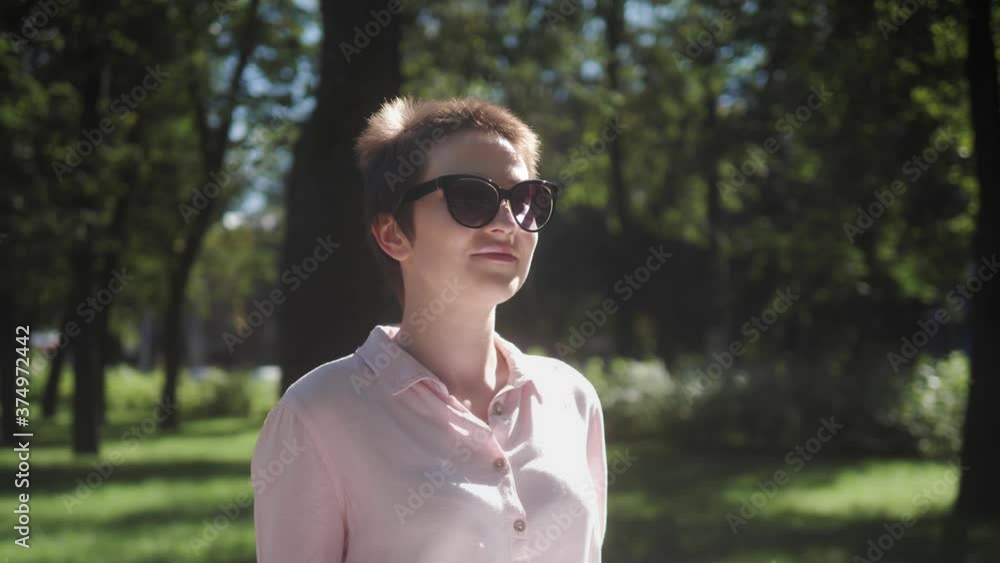 Smiling woman in sunglasses walking down street in the park having a fun. Business woman resting on a break walking on urban background. Smiling woman in sunglasses walking down street in the park having a fun. Business woman resting on a break walking on urban background.