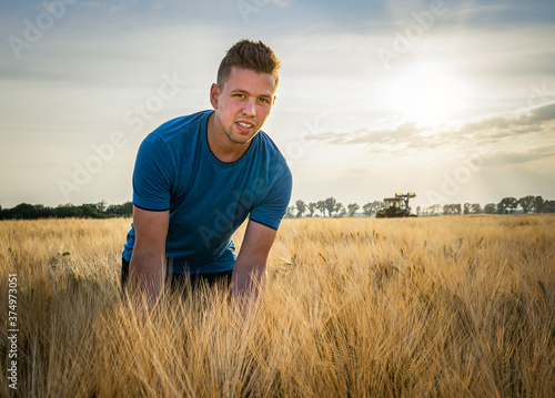 Ackerbau - junger, begeisterter Landwirt  steht im Gegenlicht der Abendsonne im goldgelben Getreidefeld. 