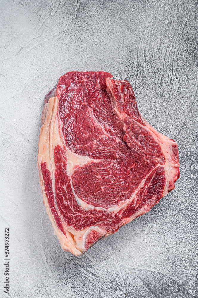Raw cowboy steak or rib eye on the bone. Marble beef. Gray background. Top view