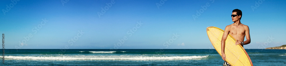 Surfer holding a surf board on tropical beach. Man with surfboard looking on caribbean sea