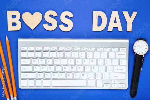 Wooden text Boss Day with pencils, wrist watch and keyboard on blue background