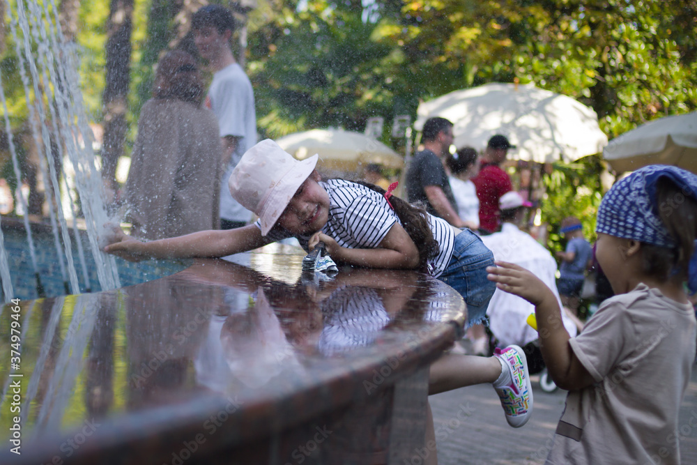 a little girl plays in the summer in the city fountain