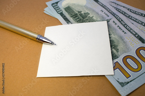 On a brown background are dollars on which is a white sheet of paper and a Golden pen. Business concept with copy space.