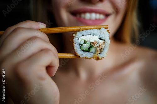 Beautiful girl eating sushi close-up. woman holding sushi roll with chopsticks. Healthy Japanese food.