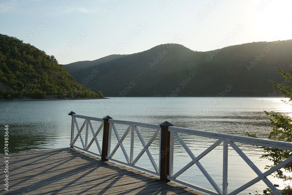 beautiful wooden pier on the Abrau Dyurso mountain lake against the background of mountains covered with dense vegetation and blue sky in the evening before sunset