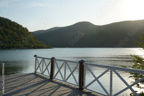 Fototapeta Naklejka Na Ścianę i Meble -  beautiful wooden pier on the Abrau Dyurso mountain lake against the background of mountains covered with dense vegetation and blue sky in the evening before sunset
