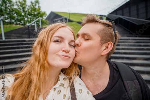 Joyful young loving couple making selfie on camera. Man kiss woman