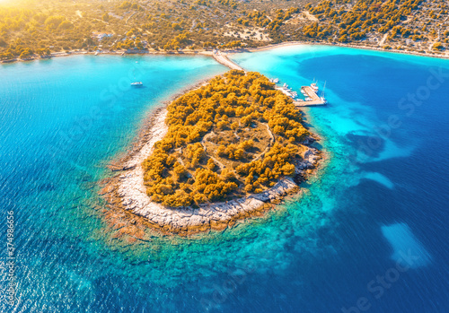 Fototapeta Naklejka Na Ścianę i Meble -  Aerial view of beutiful small island in sea bay at sunset in autumn in Murter, Croatia. Top view of clear blue water, orange trees, mountain, sandy beach, boats and yachts in fall. Tropical landscape