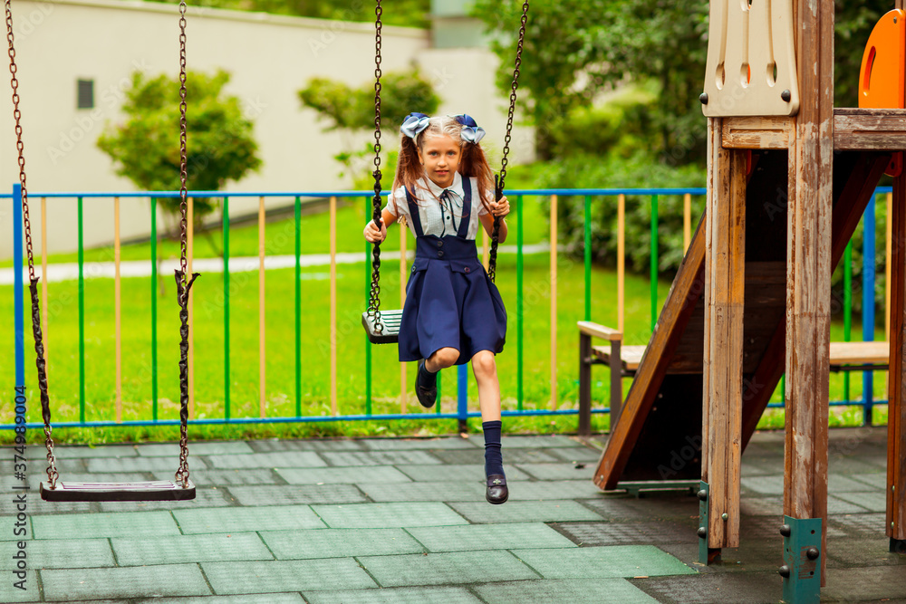 schoolgirl in school uniform, swinging on a swing in a children's Park schoolgirl in school uniform, swinging on a swing in a children's Park