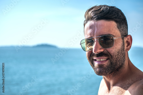 Portrait of a real man, with some white hair, some wrinkles, and sunglasses, facing the sea.