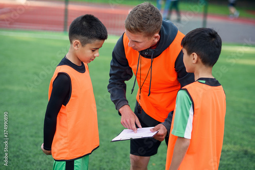 Professional soccer coach tells the strategy of football game to his attentive teen players at stadium during training.