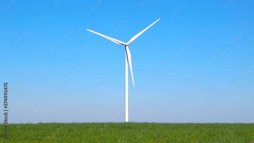 Wind turbine spinning slowly in a green grass field and bright blue sky Wind turbine spinning slowly in a green grass field and bright blue sky